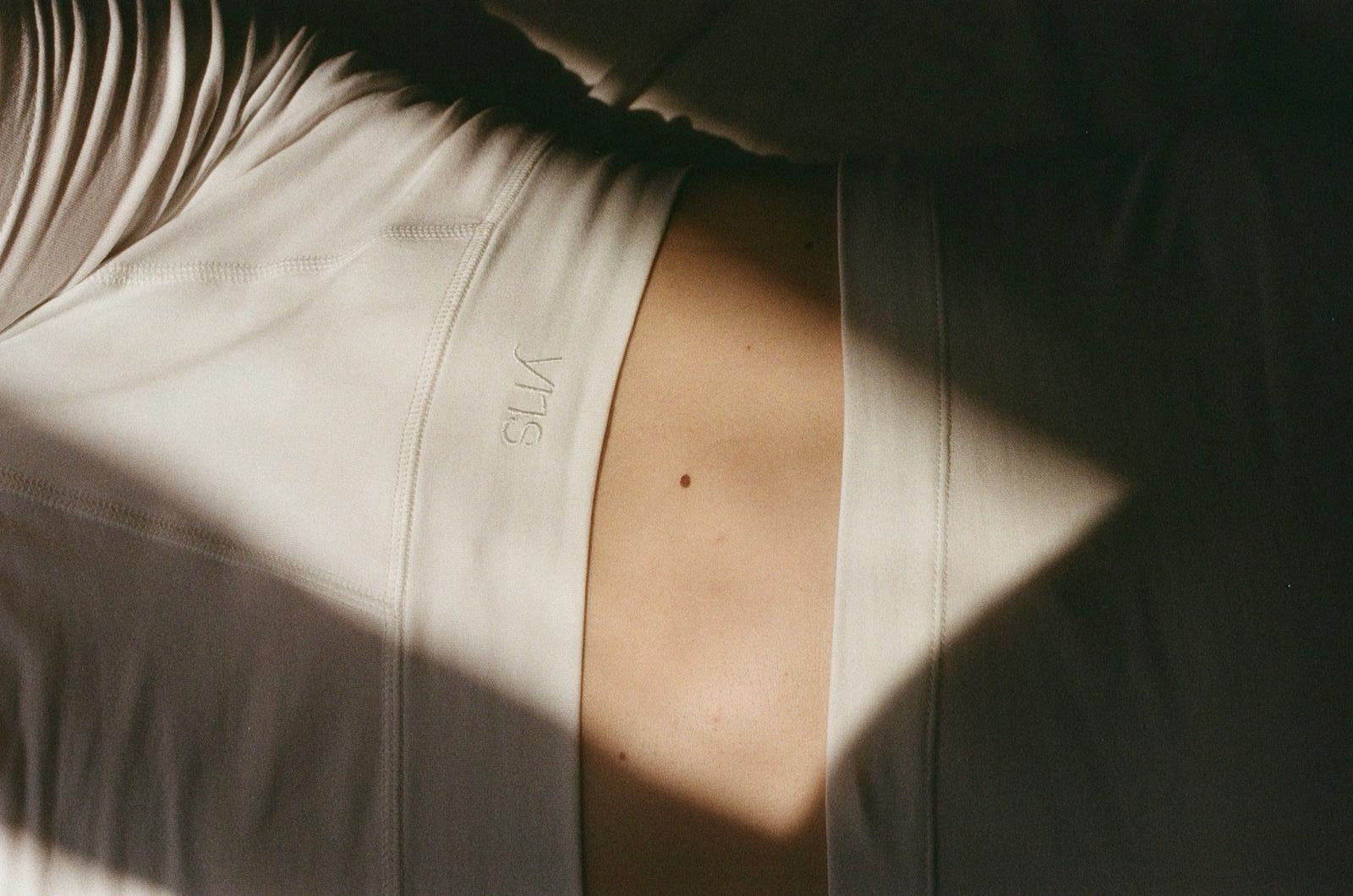 Close-up of a person wearing white boxershorts with a visible waistband and a small logo reading 'yris' in the middle photographed in dramatic directional light with strong shadows.